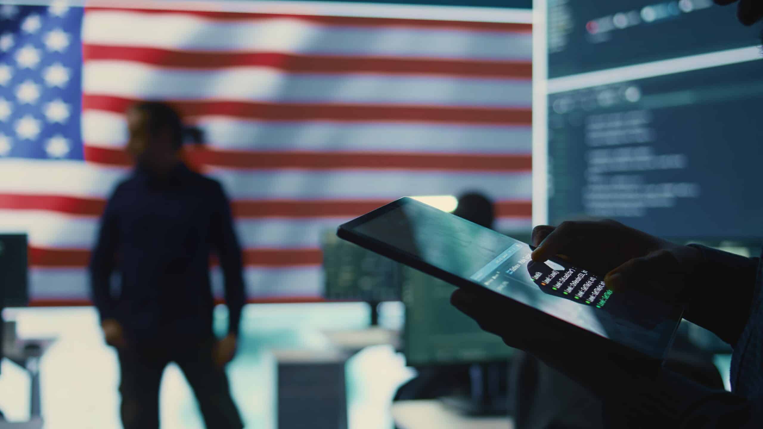IT professional using a tablet in a secure environment with the U.S. flag in background