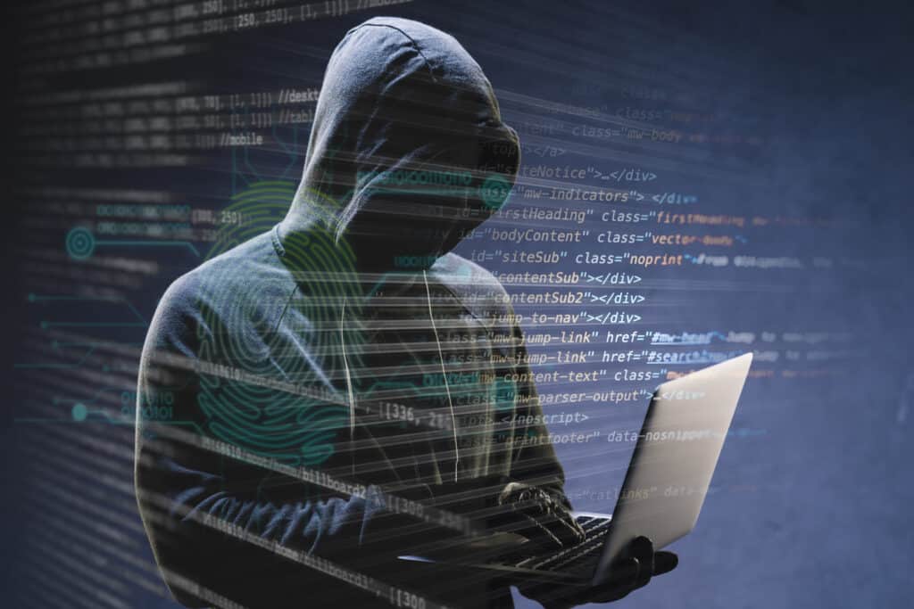 Hacker in hoodie using a laptop overlaid with code and biometric graphics